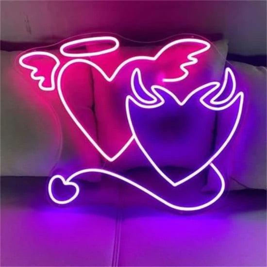 Neon Angelo e demone cuore sign glowing pink and purple heart shapes with angel wings and devil horns mounted on wall or plexiglass