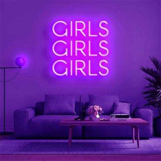 Neon sign with bright purple "GIRLS GIRLS GIRLS" text mounted on wall above sofa