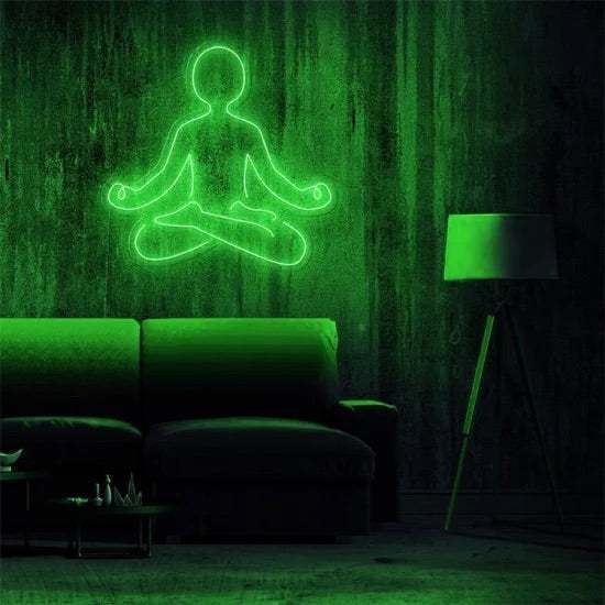 Green neon light sign of a person meditating in yoga pose on a wall above a sofa with a floor lamp nearby neon yoga decoration
