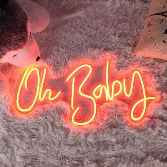 Oh Baby neon sign glowing orange on fluffy grey rug with stuffed animal and pillow nearby
