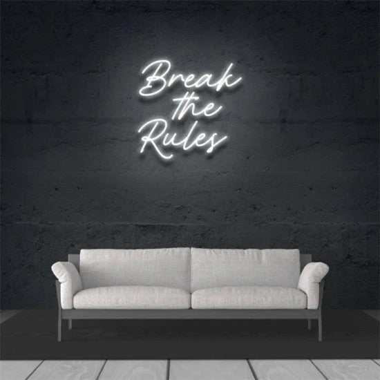 White "Break the Rules" neon sign mounted on dark wall above gray sofa