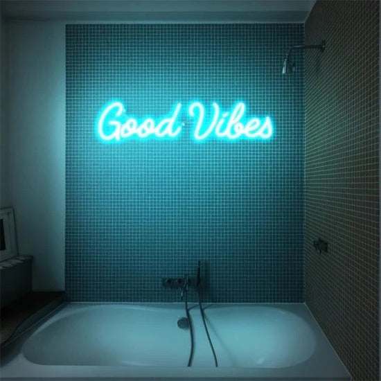 Good vibes neon sign in blue mounted on bathroom tiled wall above bathtub