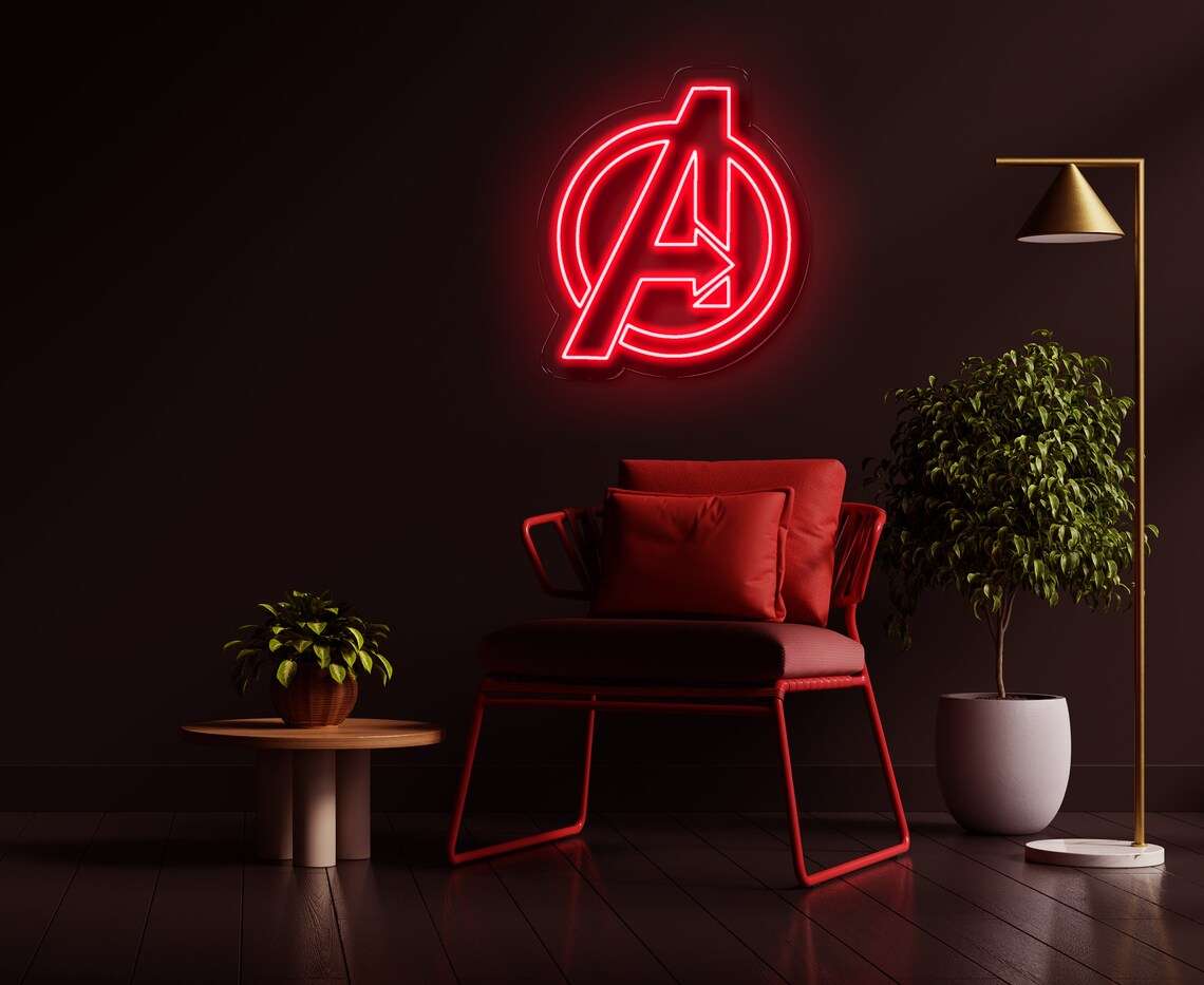 Logo neon Avengers rosso su parete scura con poltrona rossa, tavolino e pianta in vaso accanto